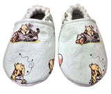 Pair of baby shoes with Winnie the Pooh illustrations on a light blue background